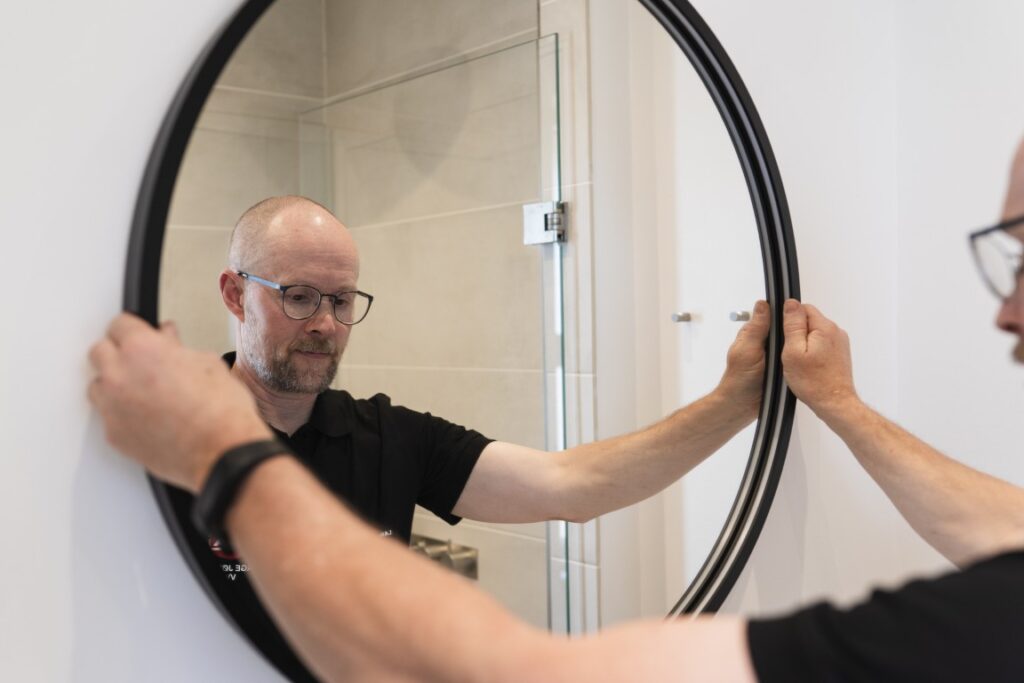 VVS-installatør monterer spejl i nyt badeværelse med moderne løsning